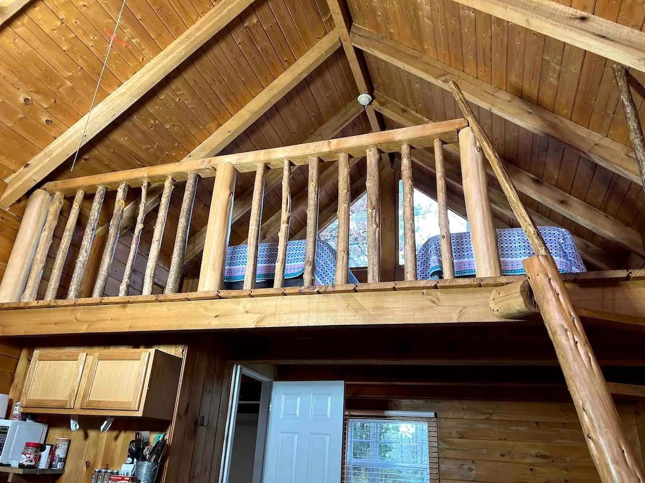 Ein Schlafzimmer im Chalet-Stil mit schrägen Wänden, einem Balkon mit Geländer und einer Tür zu einem anderen Raum.