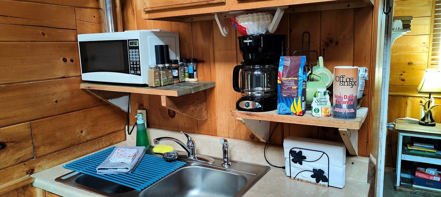Een kleine keuken met een magnetron, koffiezetapparaat en planken met keukengerei.