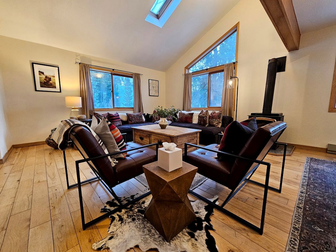Un salon chaleureux avec une cheminée, des canapés en cuir, une table basse et une grande fenêtre.
