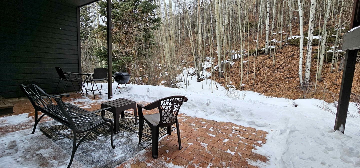 An outdoor patio with a brick floor, metal chairs, and a table.