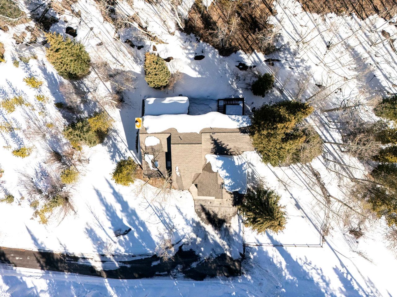 An aerial view of a house surrounded by snow-covered ground, with trees and a clear sky.