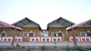 A symmetrical building with two identical wings, each with a pitched roof and a central entrance. - Vrinda Tapovan Farmstay (Chhata)