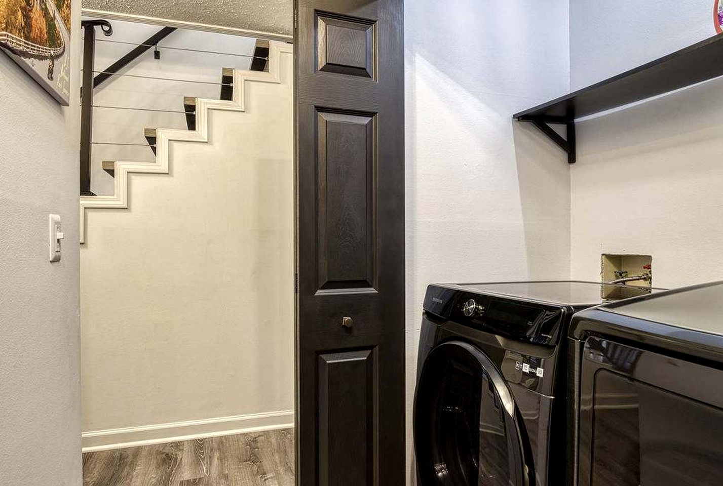 A laundry area with a washing machine and dryer, a dark wooden door, and a staircase with white walls.
