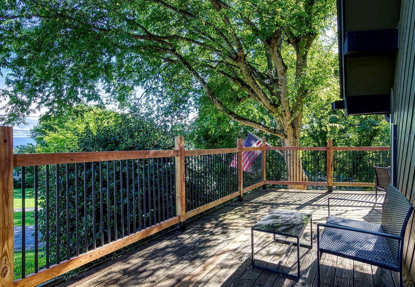 A wooden deck with a metal railing, a bench, and a flag.