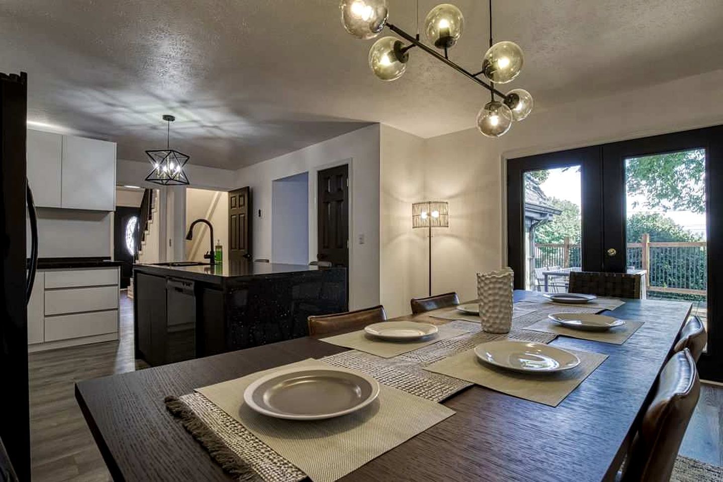 A modern kitchen with a central island, dining area with a long table, and a view of the outdoors.