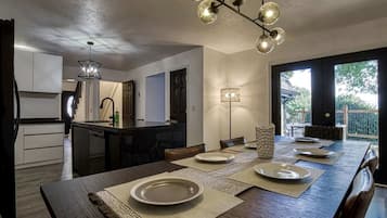 A modern kitchen with a central island, dining area with a long table, and a view of the outdoors.
