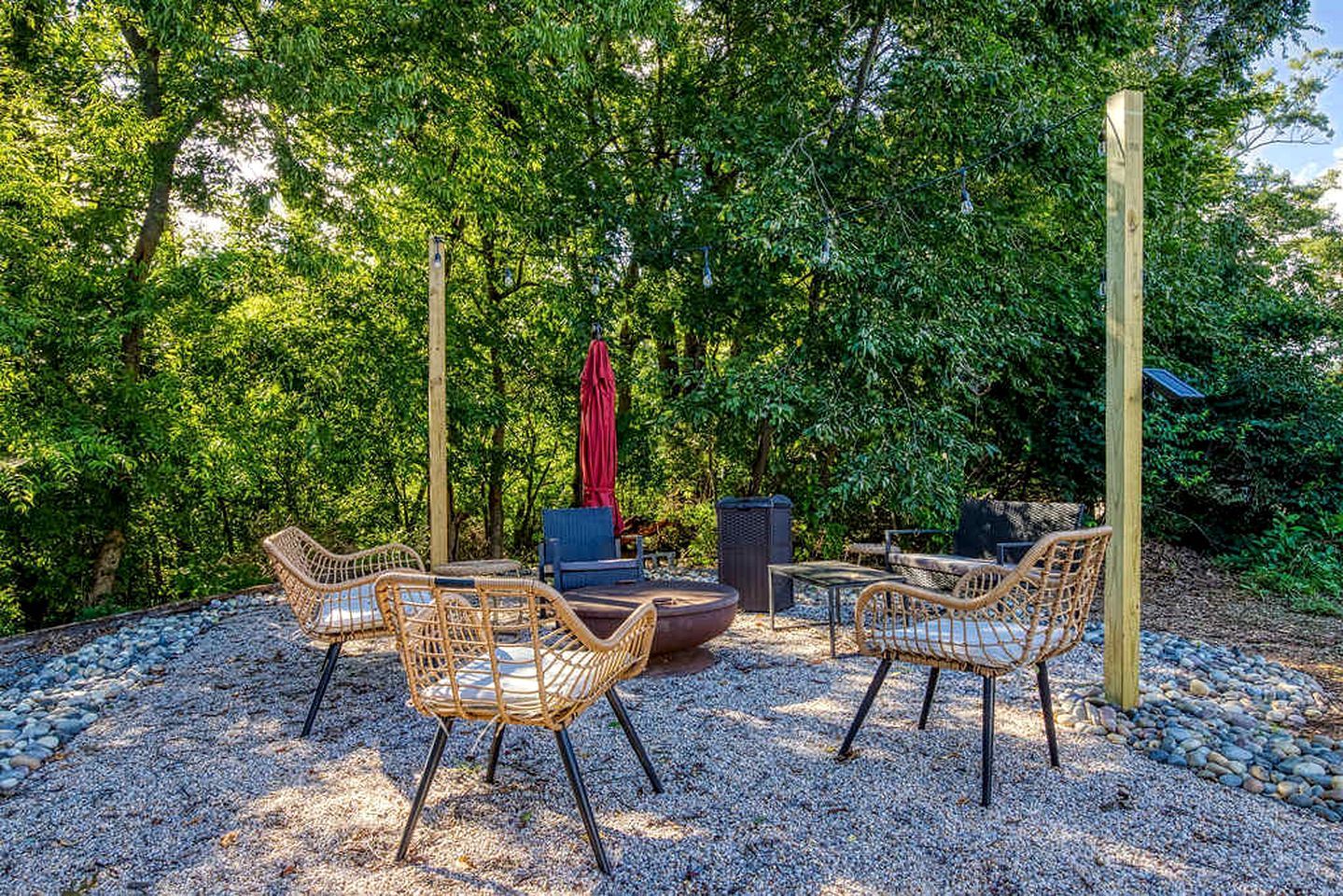 An outdoor seating area with wicker chairs, a fire pit, and a red umbrella.