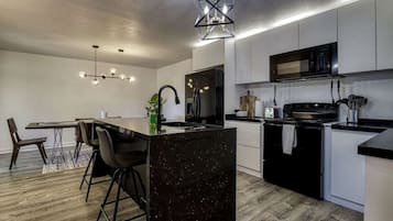 Une cuisine moderne dotée d’un îlot central, de tabourets de bar, d’une table à manger et d’un lustre.