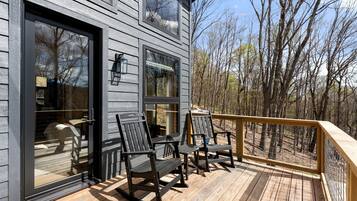 A wooden deck with outdoor seating, a railing, and a view of a forest.