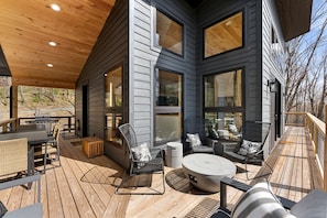A covered outdoor deck with a grill, seating area, and large windows. - Modern Mountain Retreat with Hot Tub in Lost City, West Virginia (Lost City)
