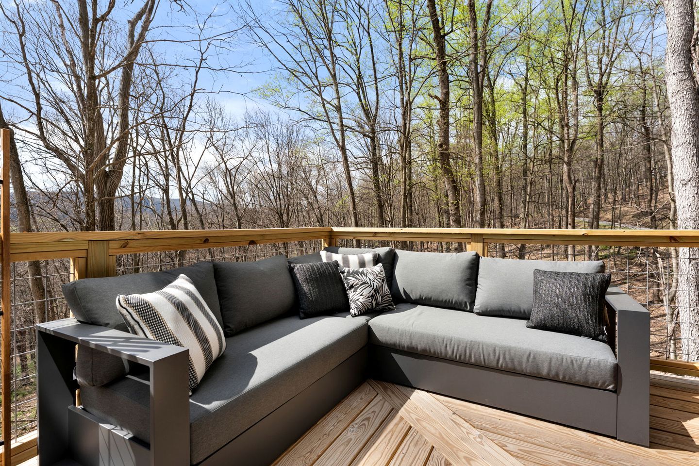 Ein Ecksofa auf einer Holzterrasse mit Blick auf einen Wald.