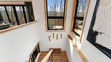 A narrow staircase with wooden railings, a view of a deck through a window, and three small potted plants on the wall.