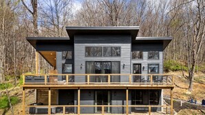 Een modern houten chalet met twee verdiepingen en een balkon, omringd door bomen.