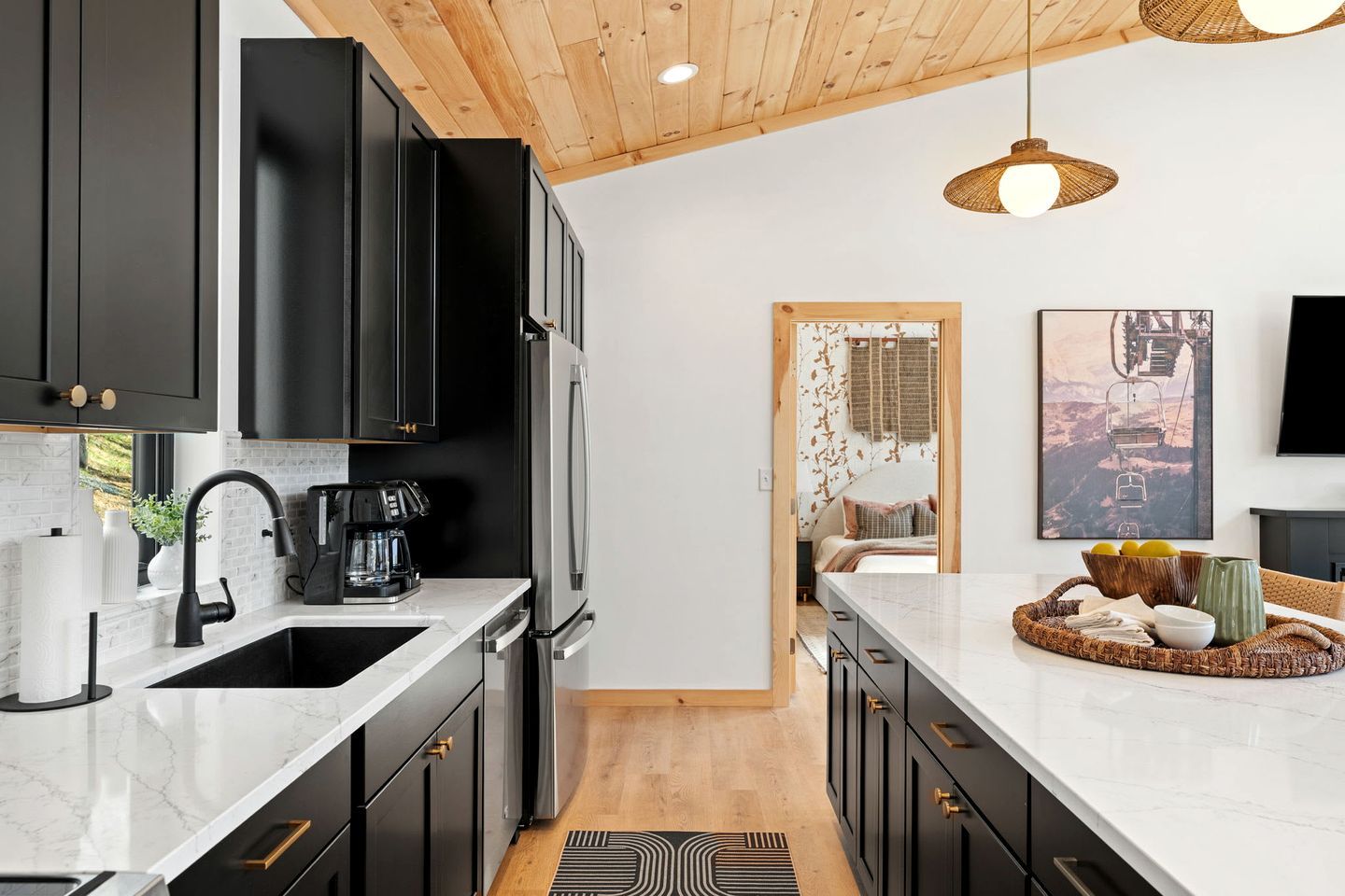 A modern kitchen with black cabinets, a stainless steel refrigerator, and a white marble countertop.