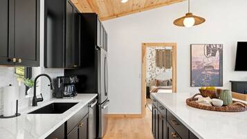 A modern kitchen with black cabinets, a stainless steel refrigerator, and a white marble countertop.