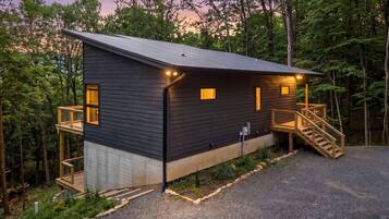 A cabin with a deck, a staircase, and a gravel driveway.