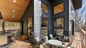 A covered outdoor deck with a grill, seating area, and large windows.