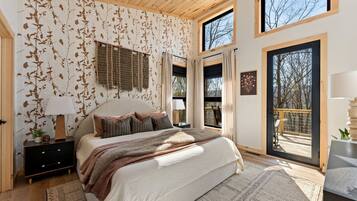 A bedroom with a large bed, a nightstand, a window with curtains, and a view of the outdoors.