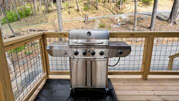 Een roestvrijstalen barbecue op een houten terras met een metalen leuning.