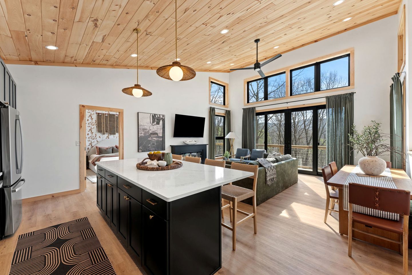 A modern kitchen with a central island, wooden ceiling, large windows, and a dining area with a view.