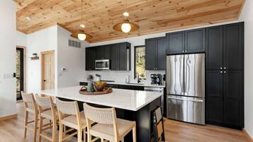 A modern kitchen with a wooden ceiling, black cabinets, stainless steel appliances, and a central island with chairs.