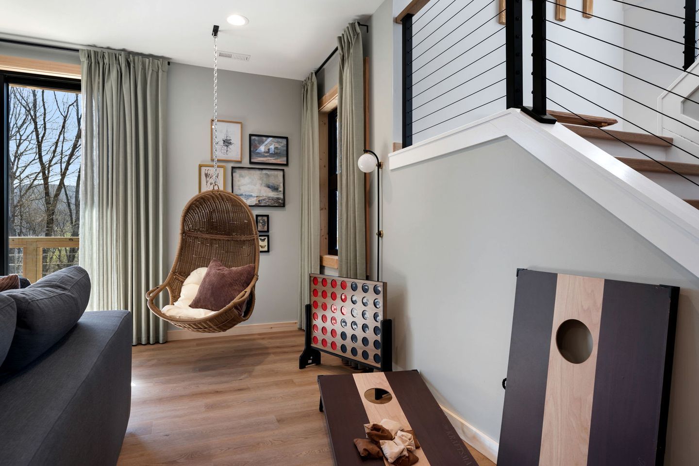 Un salon moderne avec un fauteuil suspendu, un canapé, une table en bois et un escalier.