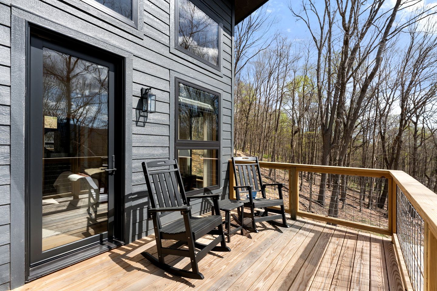 A wooden deck with outdoor seating, a railing, and a view of a forest.