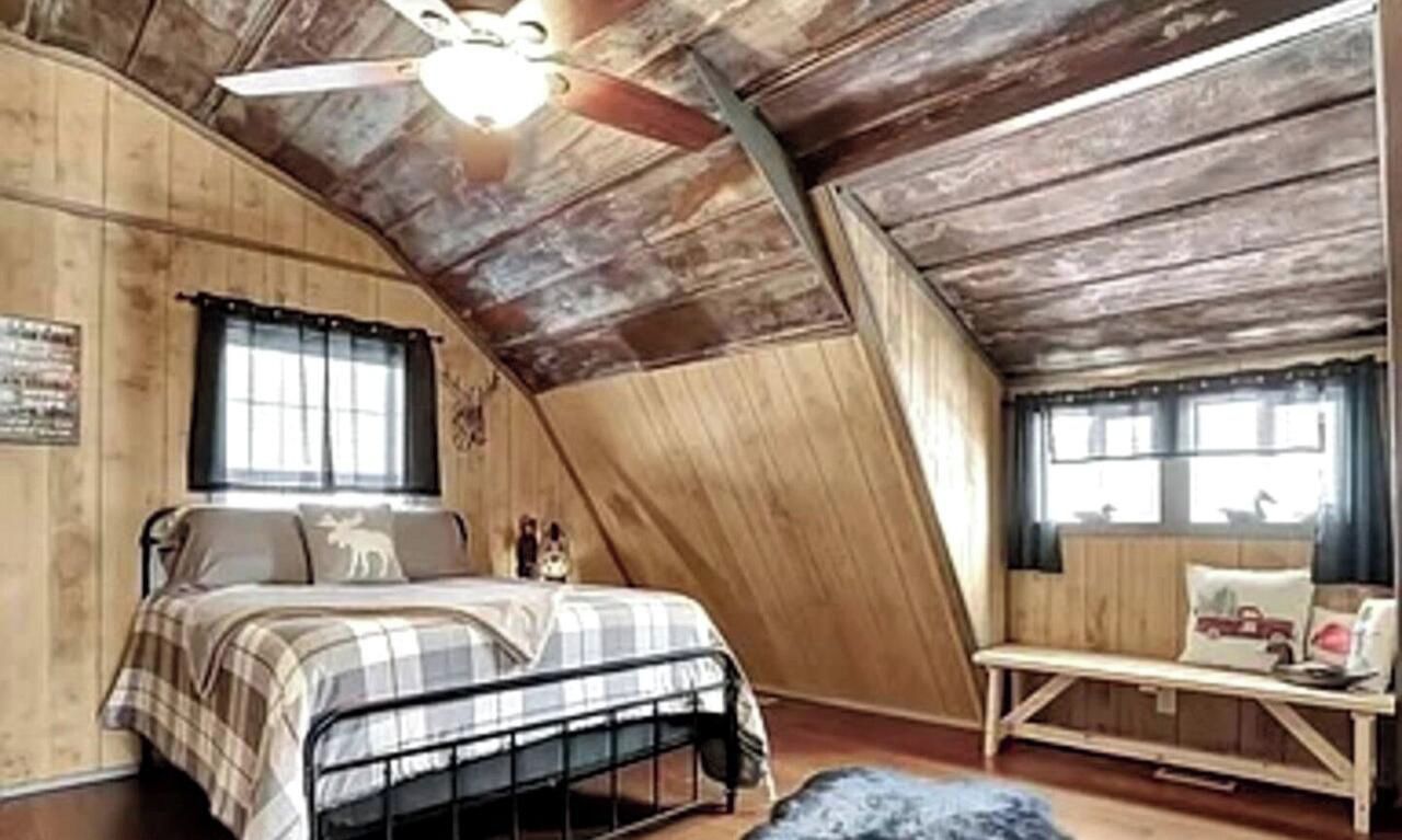 A bedroom with a sloped ceiling, a bed with a plaid bedspread, a bench with cushions, and a ceiling fan.