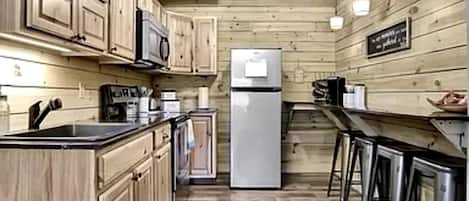 A kitchen with wooden cabinets, a refrigerator, a microwave, a sink, and bar stools.