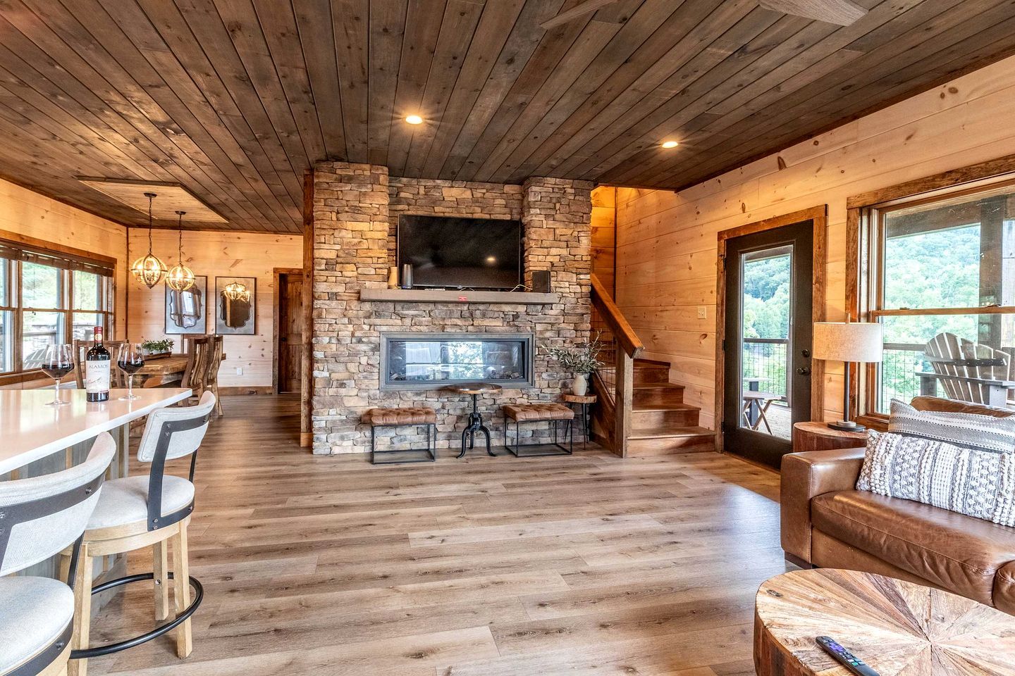 A spacious living area with a stone fireplace, wooden ceiling, and a large TV mounted above it.