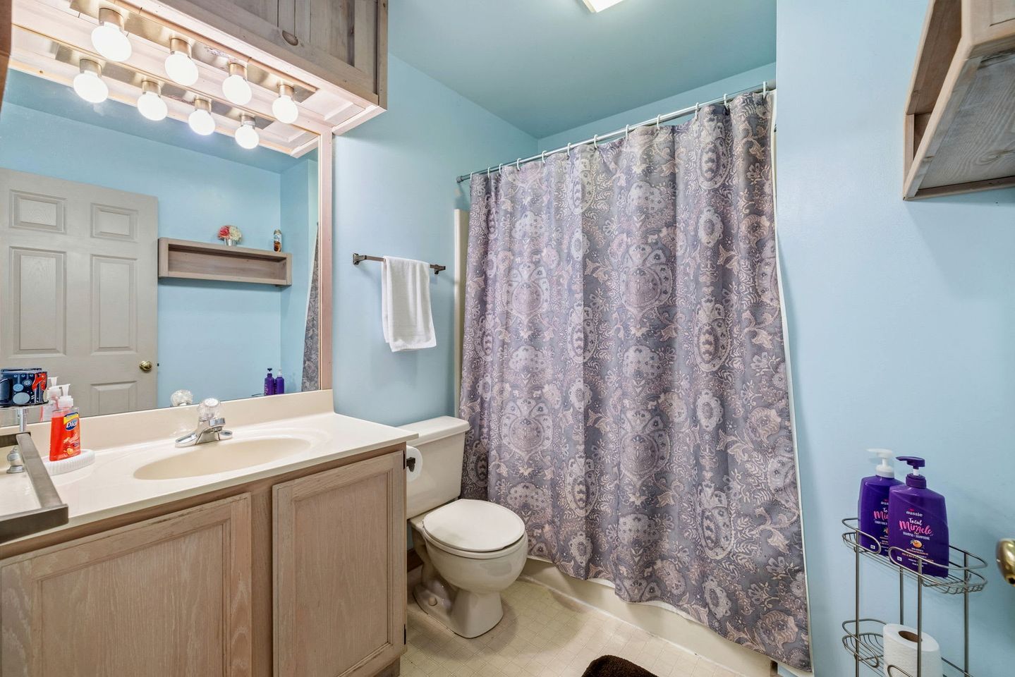 Un baño con tocador, inodoro, cortina de ducha y artículos de aseo.