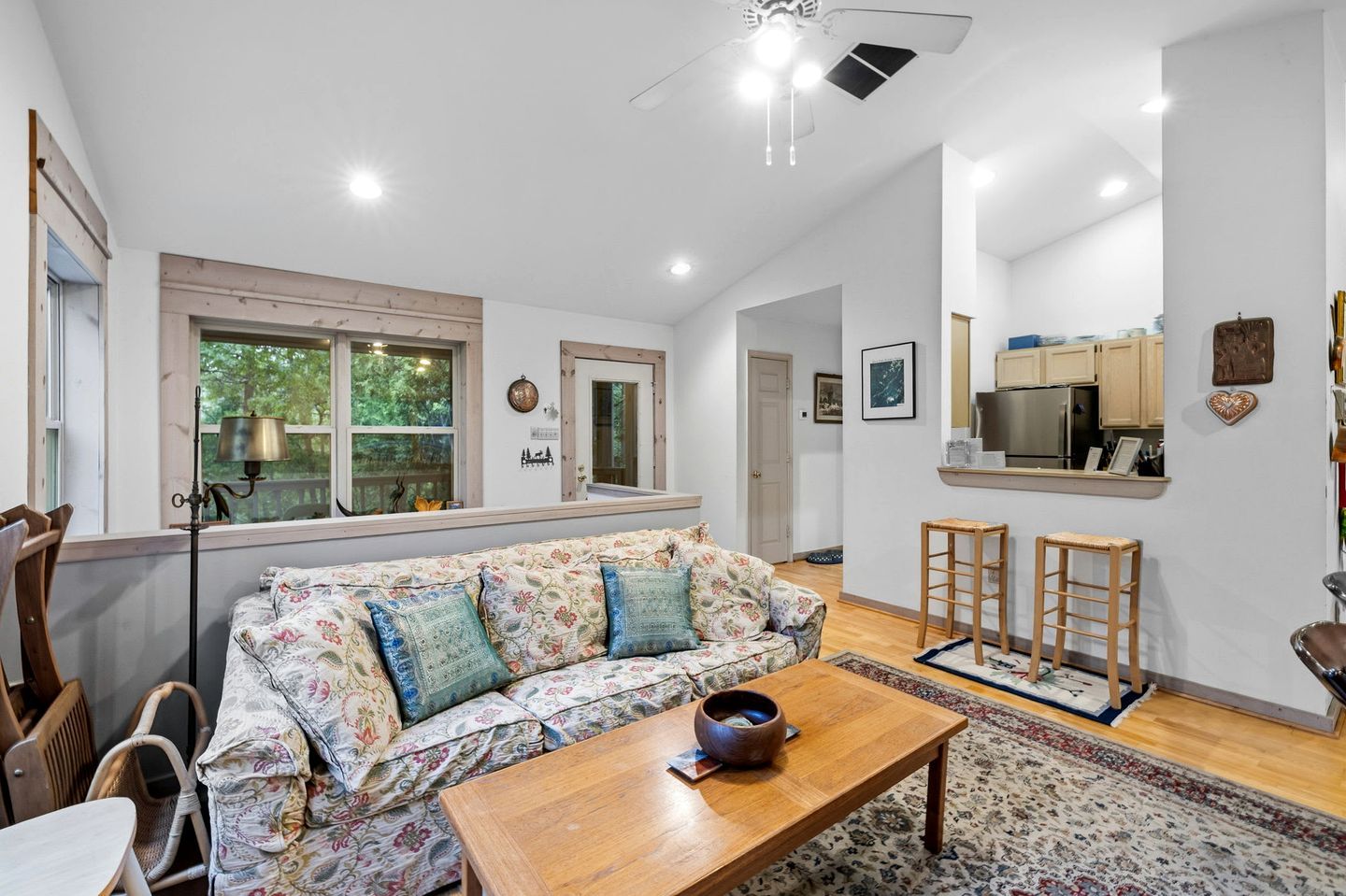 A living room with a sofa, wooden coffee table, and a kitchen area with cabinets and a refrigerator.