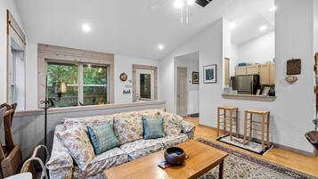 A living room with a sofa, wooden coffee table, and a kitchen area with cabinets and a refrigerator.