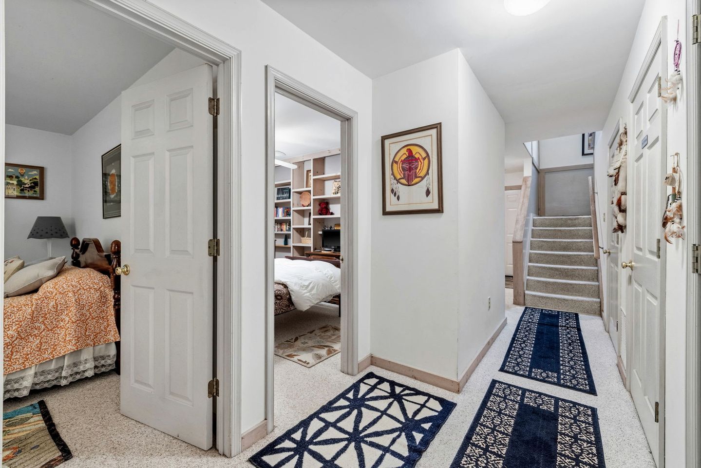 A hallway with a bed, a bookshelf, a framed picture, and a staircase.
