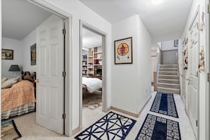 A hallway with a bed, a bookshelf, a framed picture, and a staircase. - Family Friendly Shenandoah Cabin with Fire Pit and Game Room in Basye Virginia (Basye)