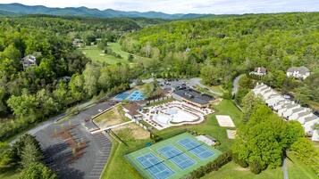 An aerial view of a golf course with a tennis court, parking areas, and residential buildings.