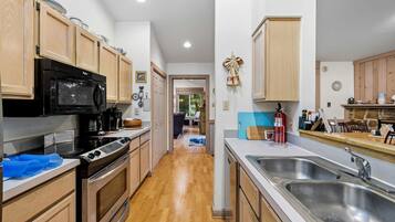 A kitchen with wooden cabinets, a black microwave, a stove, and a sink.