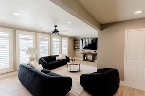 Ein Wohnzimmer mit einem schwarzen Sofa, einem Couchtisch und einem an der Wand befestigten Fernseher.