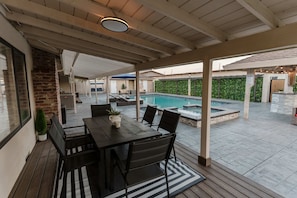 Un patio exterior con piscina, zona de estar cubierta y una mesa con sillas.