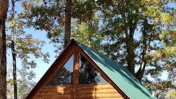 Een vakantiehuis van hout met een groen dak, een raam en een stenen fundering.