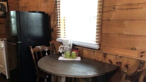 A wooden interior with a round table, chairs, a black refrigerator, and a window with blinds. - Cozy Log Cabin Retreat near Green River Lake State Park, Perfect for a Weekend of Fishing (Columbia)