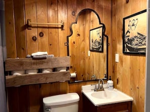 Ein Badezimmer mit Holzwandverkleidung, Toilette, Waschbecken, Handtuchhalter und gerahmten Bildern.
