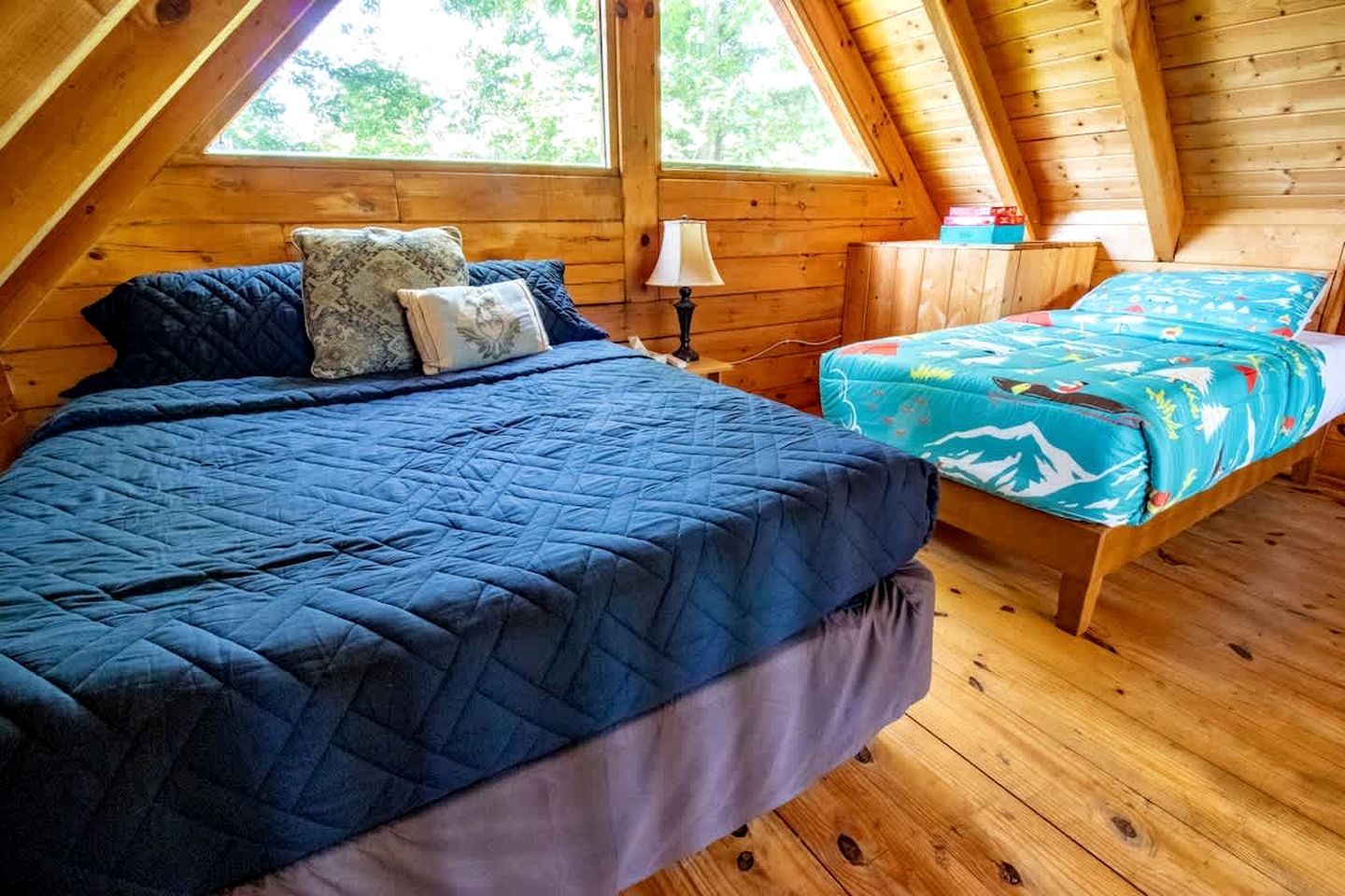 A room with a bed, a smaller bed, a nightstand, a lamp, and a window.
