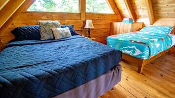 A room with a bed, a smaller bed, a nightstand, a lamp, and a window.