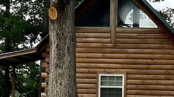 Une cabane en rondins avec un toit à deux versants, une fenêtre et un tronc d’arbre sur la gauche.