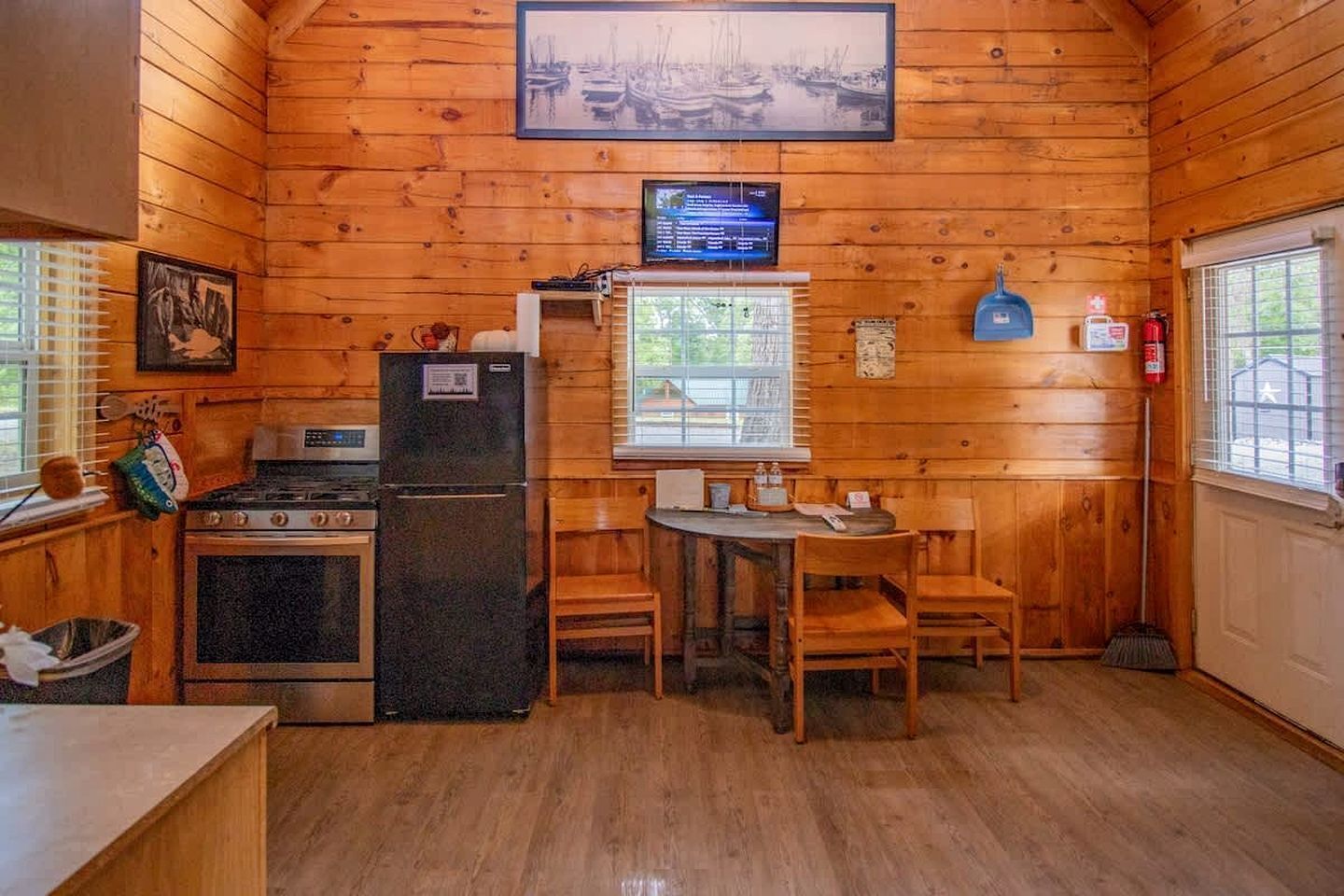 A cabin with a kitchen area, a dining table with chairs, a stove, a refrigerator, and a window with blinds.