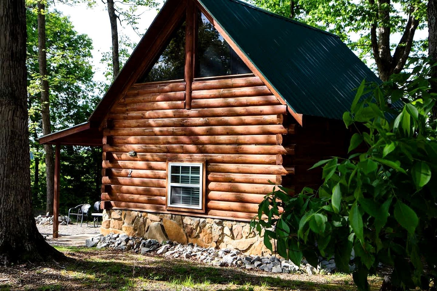 A log cabin with a stone foundation, a window, and a porch.