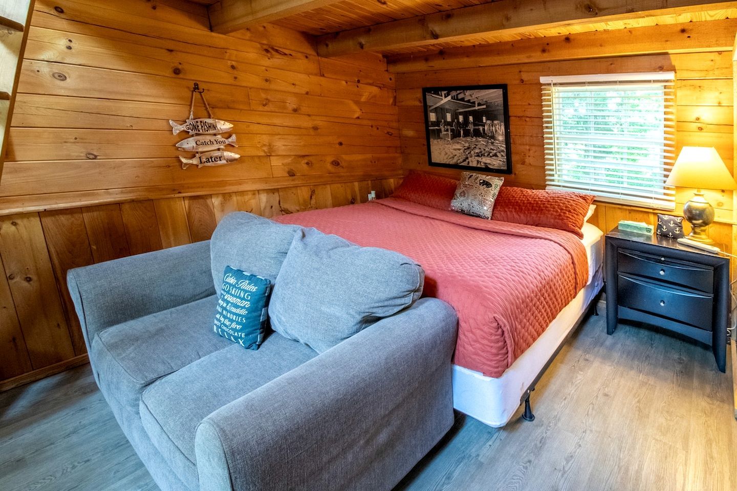 Una habitación acogedora tipo cabaña, con una cama, un sofá, una mesita de noche y un cuadro colgado en la pared.