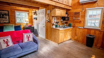 A cozy cabin interior with a sofa, a kitchen area, and wooden walls.