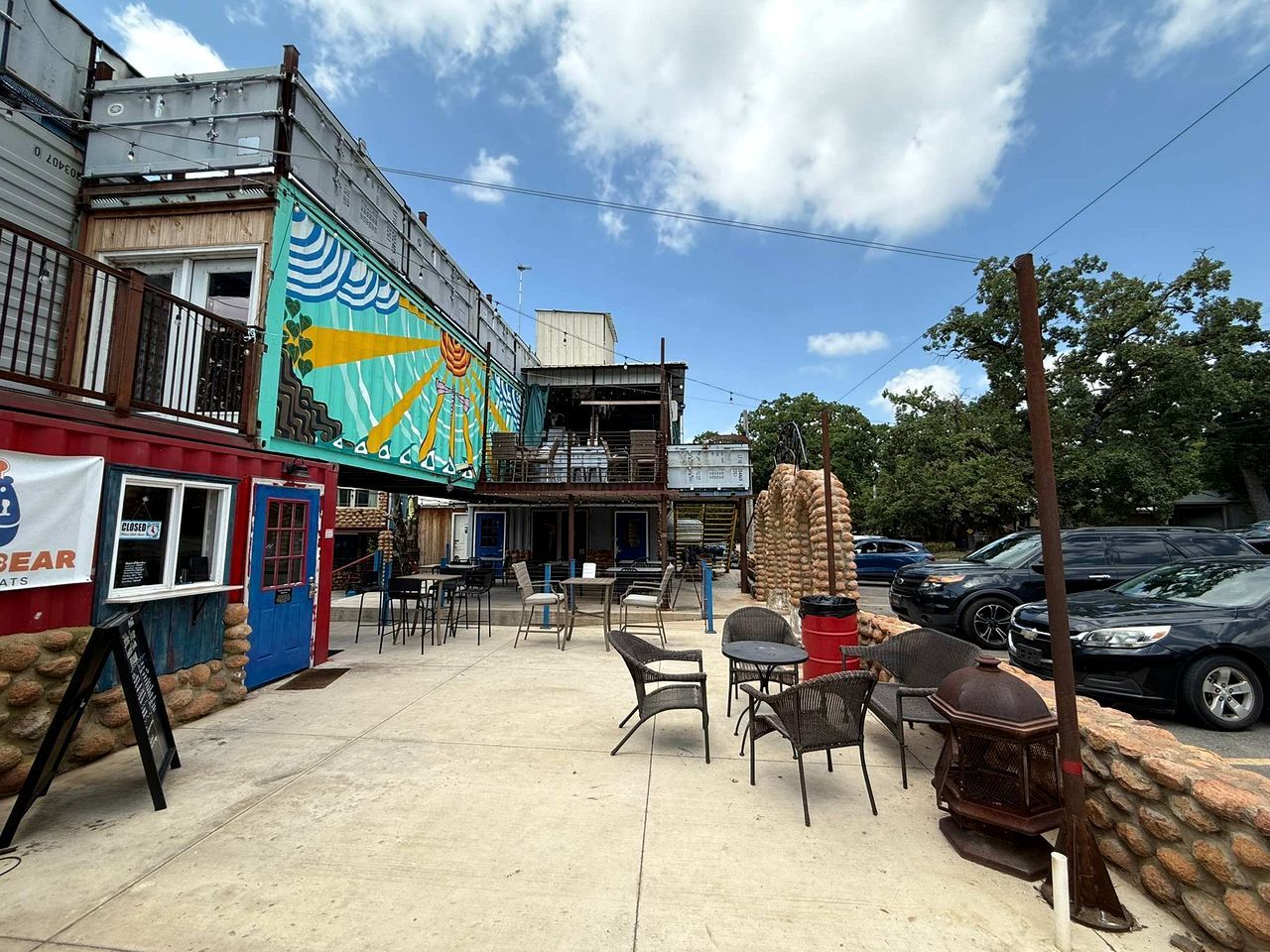 An outdoor seating area with tables and chairs, a blue door, and a colorful mural on the building.